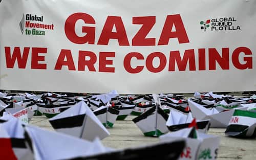 A flotilla of paper boats are laid on the ground near a banner reading "Gaza We are Coming" during a demonstration in support of Gaza and Palestinian people at Venice Lido during the 82nd Venice International Film Festival, on August 30, 2025. (Photo by Stefano RELLANDINI / AFP)