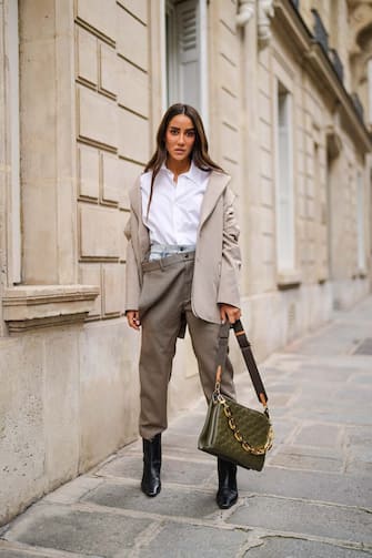 PARIS, FRANCE - APRIL 30: Tamara Kalinic wears gold earrings, a gold chain pendant necklace, a Saint Laurent white shirt, a beige oversized Y/Project blazer jacket, a shiny Khaki green leather monogram-embossed puffy lambskin Louis Vuitton Coussin MM shoulder bag, blue faded denim jeans on the top and brown suit Y/Project pants, black shiny leather western pointed heels Khaite ankle boots, on April 30, 2021 in Paris, France. (Photo by Edward Berthelot/Getty Images)