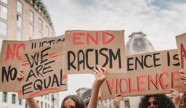 People are marching on strike against racism in the city. They are holding cardboard signs.
