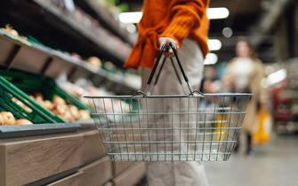 Lower section of young woman standing next to product aisle and choosing vegetables in the store. Young Asian woman doing grocery shopping in supermarket.