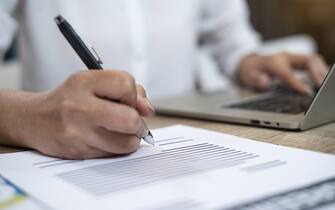 Close up of hand asian businesswoman writing on paper and using laptop  for working.