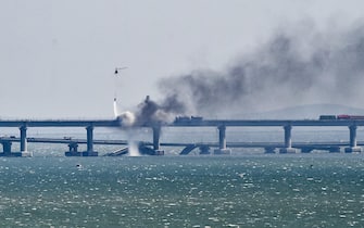 epa10230633 A firefighter helicopter pours water on fire on a collapsed part of the Kerch Strait bridge in Crimea, 08 October 2022. According to Russian authorities, "an explosion was set off at a cargo vehicle on the motorway part of the Crimean bridge on the side of the Taman peninsula, which set fire to seven fuel tanks of a train that was en route to the Crimean peninsula. Two motorway sections of the bridge partially collapsed."  EPA/STRINGER