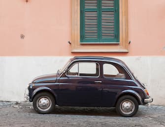 Side view of a small, classic Italian car (a vintage Fiat 500) on a cobbled backstreet in Rome.