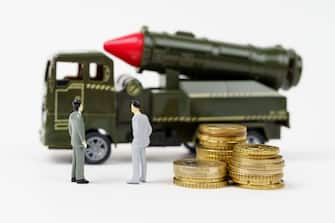 The concept of the military budget. On a white surface are figurines of people, coins and a toy military vehicle.