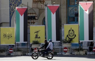epa10923625 Two persons on a motorcycle ride past large Palestinian flags hanging next to Hamas (R) and Hezbollah (C) logos in 'Palestine Square', in Tehran, Iran, 17 October 2023. Iranian supreme leader Ayatollah Ali Khamenei on 17 October 2023 warned Israel to stop the attack on Gaza, saying 'if the crimes continue, no one will be able to stop the Muslims and the Resistance forces'. Thousands of Israelis and Palestinians have died since the militant group Hamas launched an unprecedented attack on Israel from the Gaza Strip on 07 October 2023, leading to Israeli retaliation strikes on the Palestinian enclave.  EPA/ABEDIN TAHERKENAREH