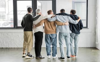 Back view of interracial men hugging during anonymous alcoholics meeting in rehab center,stock image