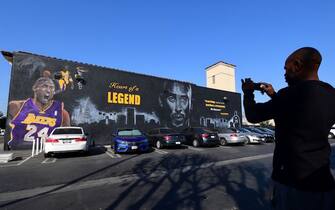 A passerby stops to photograph a huge mural in honour of the late Kobe Bryant by artist PeQue Brown in the south Los Angeles, California neighborhood of Watts on February 14, 2020, a day after it was unveiled. - The 65 x 28 foot mural features multiple images of Bryant, including one with his daughter and the names of all the victims of the fateful January 26 helicopter crash. The former Los Angeles Laker and NBA star was buried in a private ceremony with his daughter on February 7 with a Kobe Bryant Memorial set for Monday February 24 at Staples Center. (Photo by Frederic J. BROWN / AFP) (Photo by FREDERIC J. BROWN/AFP via Getty Images)