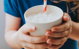 Cute little pre-school age girl gripping a cup of milk and sucking from a red striped straw. Space for copy.