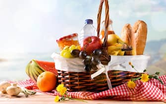 Picnic wicker basket with food on wood table on the beach with blue sky background and sun. Picnic concept. Front view. Horizontal composition.