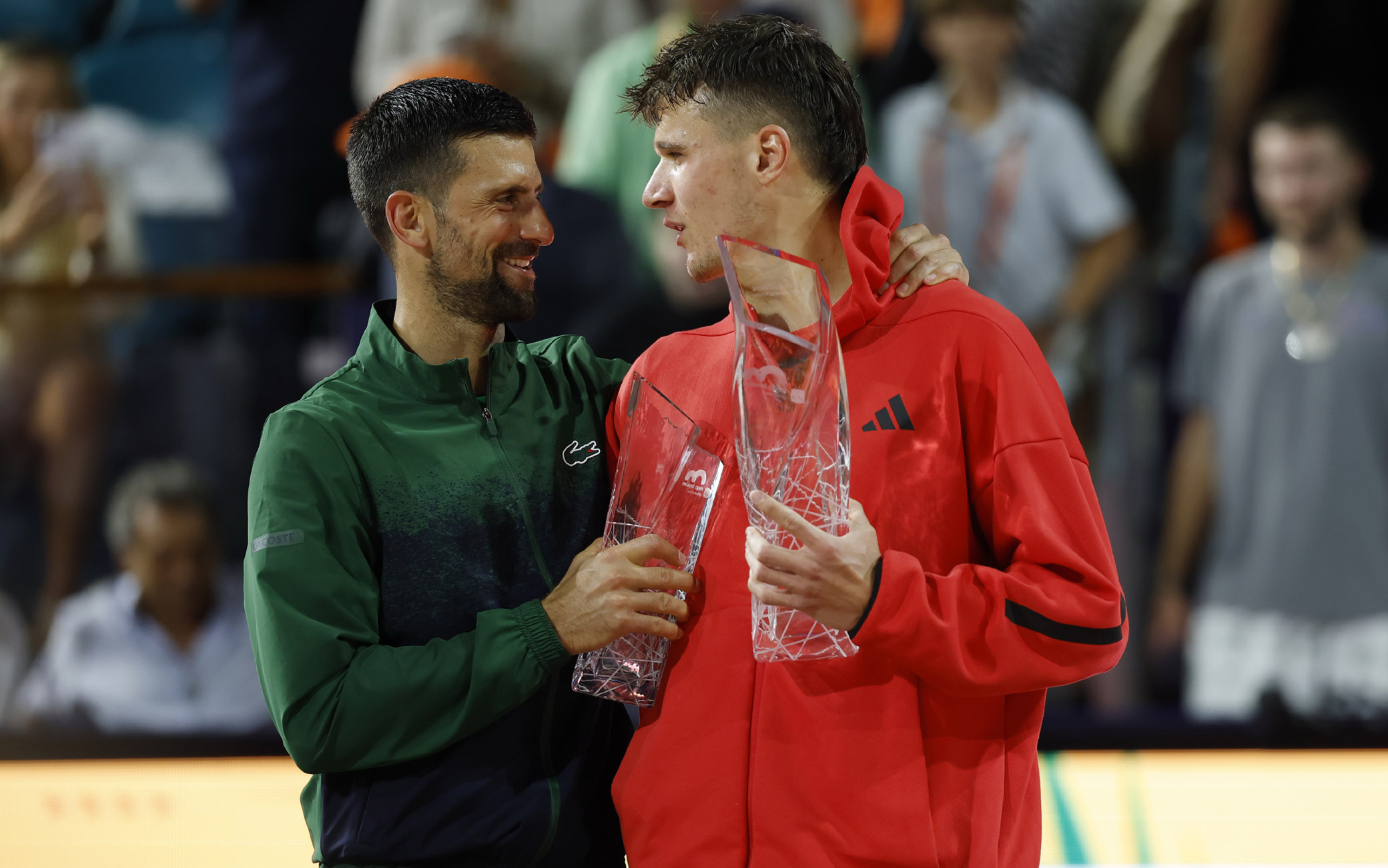 Mar 30, 2025; Miami, FL, USA; (L-R) Novak Djokovic (SRB)  hugs Jakub Mensik (CZE) while holding the finalist and Butch Buchholz championship trophies, respectively, after their men's singles championship of the Miami Open at Hard Rock Stadium. Mandatory Credit: Geoff Burke-Imagn Images/Sipa USA