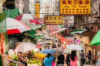 Hong Kong iStockalypse.  Shoppers with umbrellas walk through a busy outdoor food market in Sheung Wan District, Hong Kong, China