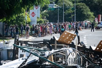 People wait in line to buy provisions from a supermarket along a street blocked by debris and burnt out items following overnight unrest in the Magenta district of Noumea, France's Pacific territory of New Caledonia, on May 18, 2024. Hundreds of French security personnel tried to restore order in the Pacific island territory of New Caledonia on May 18, after a fifth night of riots, looting and unrest. (Photo by Delphine Mayeur / AFP) (Photo by DELPHINE MAYEUR/AFP via Getty Images)