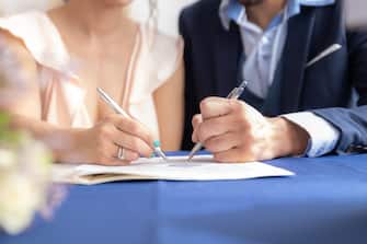 Close-up view of man and woman signing marriage certificate, she wears a vintage wedding dress and he wears a formal suit. Beginning of life as a couple, with a promise to be together forever.