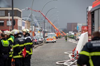 epa10566218 Firefighters gather at the scene of a fire burning at a warehouse in the Rothenburgsort district of Hamburg, Germany, 09 April 2023. Residents have been warned of heavy smoke and possible toxins in the air. An alert issued by the Hamburg fire department said smoke gasses and chemical components in the air could affect breathing.  EPA/DOMINICK WALDECK