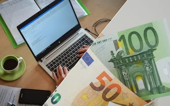 Un computer utilizzato da un uomo e alcune banconote da 50 e 100 euro