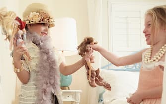 Two girls dressed up in adult fancy clothes in fairy tale bedroom happy and laughing playing with dolls