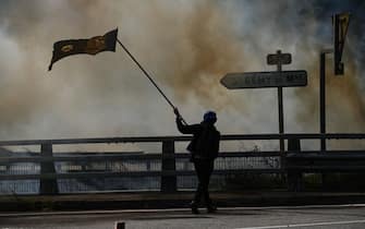 A protester waves a flag near tear gas smoke during a march on the road  at a demonstration against the construction of a high-speed rail line between Lyon and Torino, in La Chapelle, near Modane, in the French Alps' Maurienne valley, on June 17, 2023. Hundreds of oponents to the Lyon-Torino high-speed rail line demonstrated on June 17 despite a ban on the gathering, of which the details are yet to be determined and despite a heavy police presence in the valley. They set up a makeshift camp on land lent by the municipality of La Chapelle, outside the ban zone announced the day before by the Savoie prefecture. (Photo by OLIVIER CHASSIGNOLE / AFP) (Photo by OLIVIER CHASSIGNOLE/AFP via Getty Images)