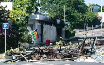A torched residence (background C) is seen on a street blocked by debris and burnt out items following overnight unrest in the Magenta district of Noumea, France's Pacific territory of New Caledonia, on May 18, 2024. Hundreds of French security personnel tried to restore order in the Pacific island territory of New Caledonia on May 18, after a fifth night of riots, looting and unrest. (Photo by Delphine Mayeur / AFP) (Photo by DELPHINE MAYEUR/AFP via Getty Images)