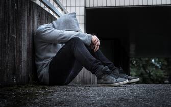 Depression, social isolation, loneliness, mental health and discrimination concept. Sad, lonely, depressed and unhappy man. Hooded person sitting.