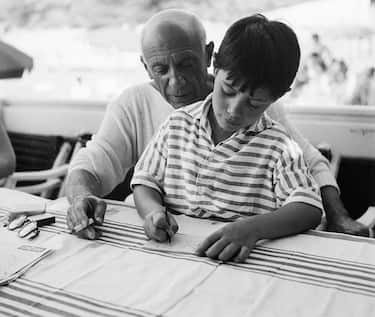 (Original Caption) 8/21/55-La Garoupe, France: Famed Spanish painter and sculptor Pablo Picasso takes sometime give his young son Claude some instruction in the rudiments of sketching and painting. So intent is the boy on following in his father's brush strokes that he's already practicing the signature he'll use on future art works.