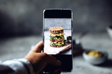 Woman using a mobile phone to take photograph of a large vegan sandwich. Woman's hand taking pictures of super sandwich on the table with his smartphone.