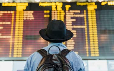Young man with hat and backpack looking at arrival departure board at the airport