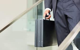 Business man carrying a cellphone and suitcase. Low section of business man carrying a cellphone and suitcase and walking down the stairs.