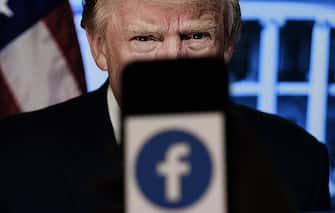 In this photo illustration, a phone screen displays a Facebook logo with the official portrait of former US President Donald Trump on the background, on May 4, 2021, in Arlington, Virginia. - Facebook's independent oversight board was set for a momentous decision on the platform's ban of former US president Donald Trump, as debate swirls on the role of social media in curbing hateful and abusive speech while controlling political discourse. (Photo by Olivier DOULIERY / AFP)