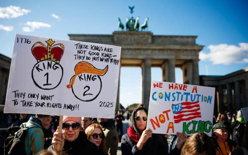 epa12462164 People hold placards reading 'We have a constitution, not a king.' (R) and 'They only want to take your rights away. These kings are not good kings - they do not want to play' (L) during a rally in front of the Brandenburg Gate in Berlin, Germany, 18 October 2025. The rally, held under the slogan 'No Kings' expressed solidarity with protests against the U.S. government and the policies of President Donald J. Trump.  EPA/CLEMENS BILAN