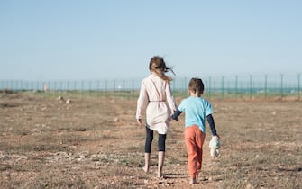 two poor children family brother and sister refugee illegal immigrant walking barefooted through hot desert towards state border with barbed fence wire