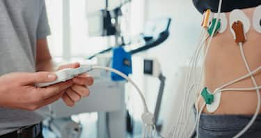 Doctor with holter monitor machine on patient stomach in hospital exam or people consulting. Hands of healthcare expert consultation with woman, medical ECG technology and heart health in cardiology