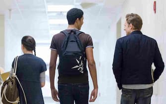 High school students walking down school corridor, rear view