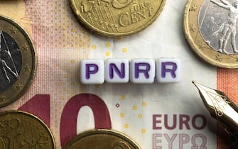 Pnrr (national recovery and resilience plan) concept: euro banknote and coins sorrounds the word pnnr