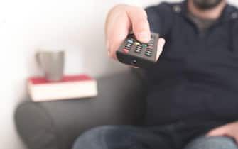 front view of person sitting on sofa using TV remote control to change channels