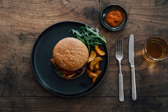 Top view of delicious cheeseburger and potato wedges, placed on the plate with knife and fork on a wooden dining table.