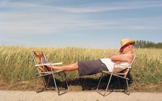 Men wearing straw hat sleeping on 2 camping chairs, by corn field