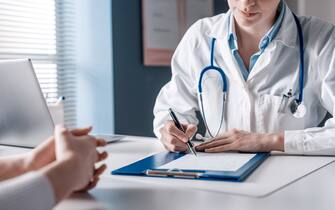 Doctor sitting at desk and writing a prescription for her patient