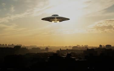 A strange flying machine in the shape of a saucer, silently hovering in the air. It emits a bright light and seems to scan the surrounding space with a beam.