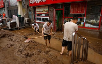 epa10779171 Men shovel mud outside a store in Mentougou District, west of Beijing, China, 01 August 2023. Heavy rains brought by Typhoon Doksuri caused floods in northern China and left two dead and thousands being evacuated as Beijing experienced its heaviest rainfall of the year.  EPA/MARK R. CRISTINO