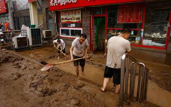 epa10779171 Men shovel mud outside a store in Mentougou District, west of Beijing, China, 01 August 2023. Heavy rains brought by Typhoon Doksuri caused floods in northern China and left two dead and thousands being evacuated as Beijing experienced its heaviest rainfall of the year.  EPA/MARK R. CRISTINO