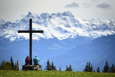 epa09223641 People take a break under a cross on a spring weather day in front of the Swiss Alps mountains (Les Dents du Midi), in Les Pleiades Blonay, above Montreux, Switzerland, 23 May 2021.  EPA/LAURENT GILLIERON