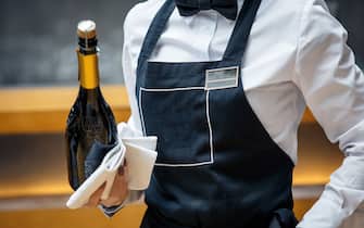 waiter in a black apron in a restaurant with a bottle of prosecco
