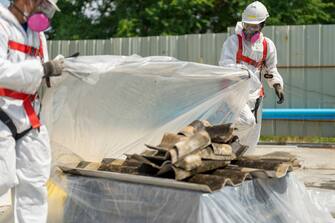 Workers wearing protective clothing while removing the asbestos roof. Hazardous waste management and working safety concept. Professional waste disposal.