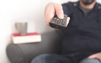 front view of person sitting on sofa using TV remote control to change channels