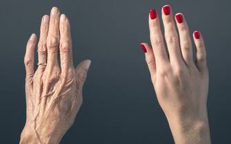 Studio photograph of elderly woman's hand beside a younger woman's hand.