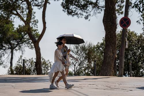 People cover themselves from the sun with hats or umbrellas due to record temperatures in Barcelona, Spain, on July 1, 2025. The Fabra Observatory reports that June 2025 is the hottest June in more than 100 years in Barcelona, breaking records since 1914. (Photo by Marc Asensio/NurPhoto via Getty Images)