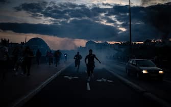 Protesters run from launched tear gas canisters during clashes with police in Lyon, south-eastern France, on June 30, 2023, three days after a 17-year-old boy was shot in the chest by police at point-blank range in Nanterre, a western suburb of Paris. French President Emmanuel Macron has announced measures including more police and urged parents to keep minors off the streets as he battled to contain nightly riots over a teenager's fatal shooting by an officer in a traffic stop. (Photo by JEFF PACHOUD / AFP) (Photo by JEFF PACHOUD/AFP via Getty Images)