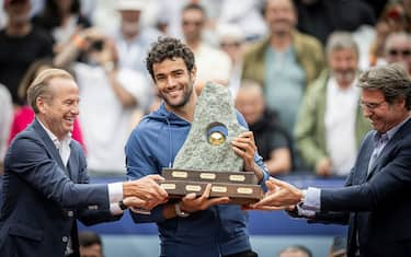 Italy's Matteo Berrettini gets help to hold up the heavy trophy made with granit, after winning the final match against France's Quentin Halys at the Swiss Open tennis tournament in Gstaad, on July 21, 2024. (Photo by GABRIEL MONNET / AFP) (Photo by GABRIEL MONNET/AFP via Getty Images)