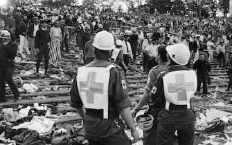 Rescuers attend 29 May 1985 victims at the scene of riots in Heysel football stadium in Brussels after thirty-nine Juventus football fans died during rioting at the European Cup Final in Brussels. The tragedy occured when a wall collapsed in the stadium and crushed Juventus fans as they tried to escape Liverpool supporters. The two sets of supporters had spent the day drinking in the Belgian city and had arrived at the Heysel stadium waving flags and chanting. Shortly before kick off the atmosphere turned violent and Liverpool supporters stampeded through a thin line of police towards the rival fans. As the Juventus fans retreated a wall collapsed under the pressure and fans were crushed and trampled to death in the panic. AFP PHOTO DOMINIQUE FAGET        (Photo credit should read DOMINIQUE FAGET/AFP via Getty Images)
