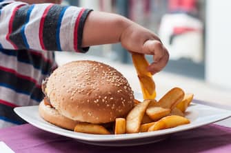closeup of little boy hand eating hamburger and french fries at restaurant